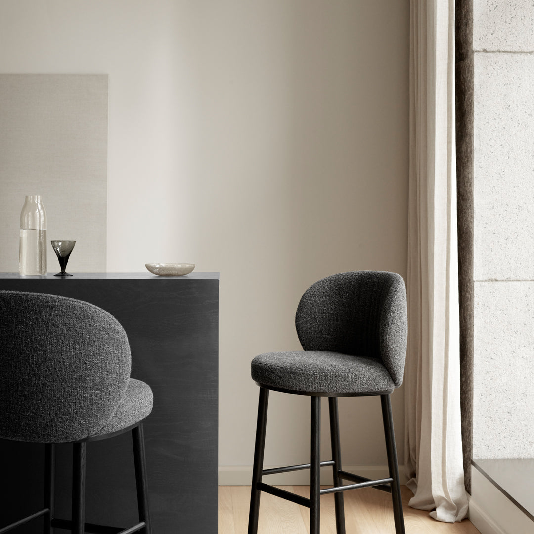 Gray upholstered bar stool with a sleek design, set against a neutral background and soft texture accents.