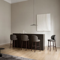 Gray upholstered bar stools with curved backs, set against a neutral wall and wooden floor in a minimalist space.