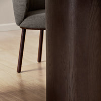 "Close-up of dark wood surface with smooth texture, complemented by a soft grey fabric chair and warm wooden floor."