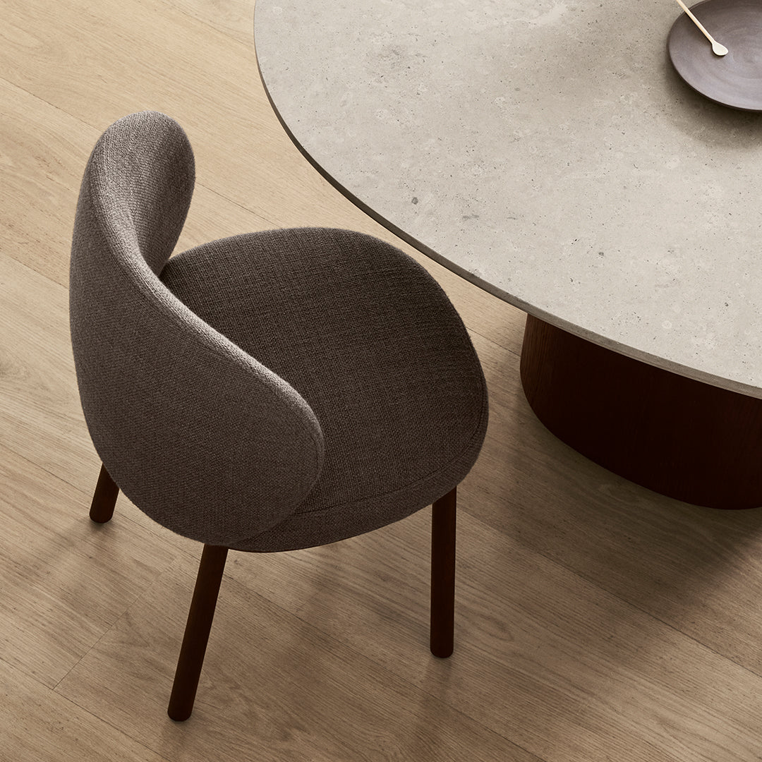 Gray upholstered chair with curved backrest, sitting beside a round stone table on a light wooden floor.