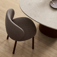 Gray upholstered chair with curved backrest, sitting beside a round stone table on a light wooden floor.