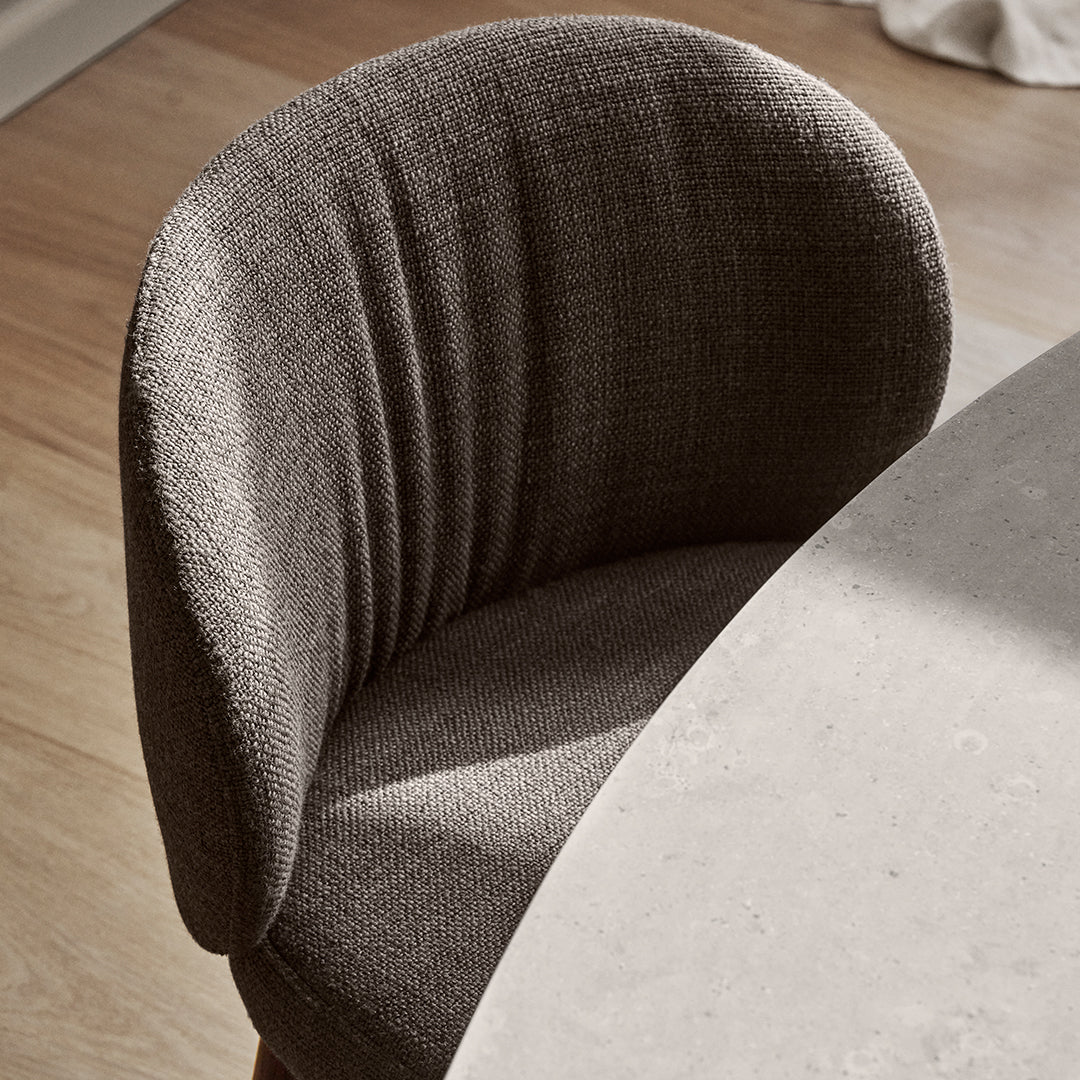Curved grey chair with textured fabric, featuring subtle vertical lines, paired with a light stone tabletop.