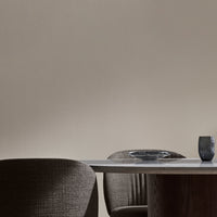 Neutral beige wall with dark brown textured chairs and a sleek wooden table, accented by a glass plate and dark tumbler.