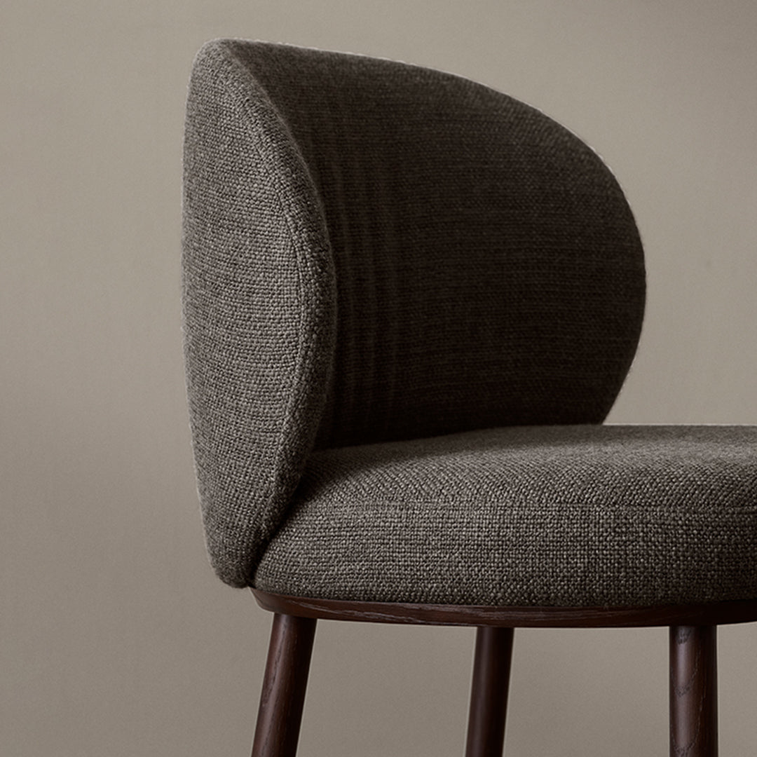 Curved gray upholstered chair with subtle texture and rich brown wooden legs against a neutral background.