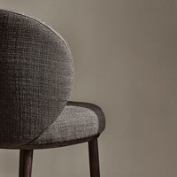 Gray textured upholstery on a modern chair with a rounded back and dark wooden legs against a neutral background.