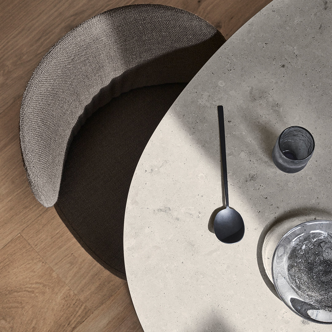 Stylish beige and dark brown chair by a light grey, round marble table, accented with matte black utensils.