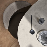 Stylish beige and dark brown chair by a light grey, round marble table, accented with matte black utensils.