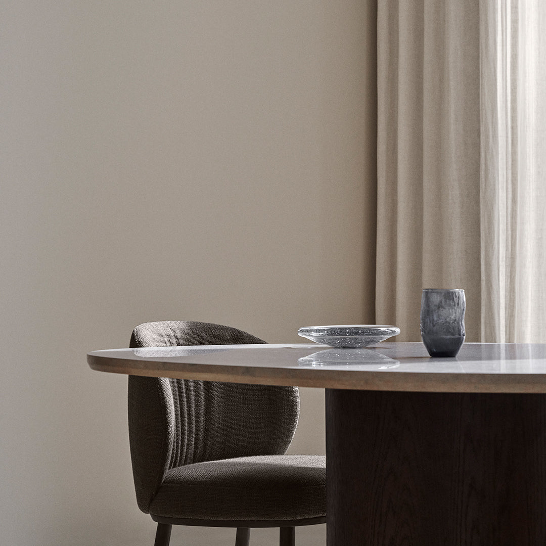 Elegant gray chair with ribbed upholstery, round wooden table, and minimalist decor against neutral wall backdrop.
