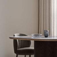Elegant gray chair with ribbed upholstery, round wooden table, and minimalist decor against neutral wall backdrop.