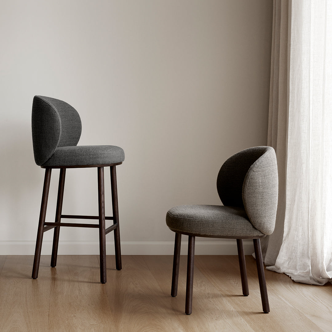 Two stylish chairs in various shades of gray with modern curved backs and wooden legs, set against a neutral backdrop.