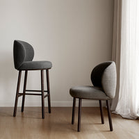Two stylish chairs in various shades of gray with modern curved backs and wooden legs, set against a neutral backdrop.