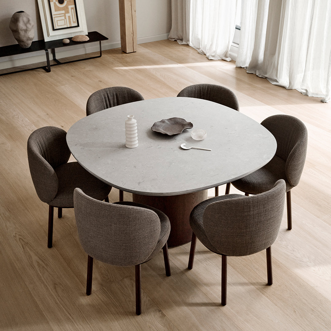 Round marble dining table with gray upholstered chairs, set on light wooden floor in a modern interior.