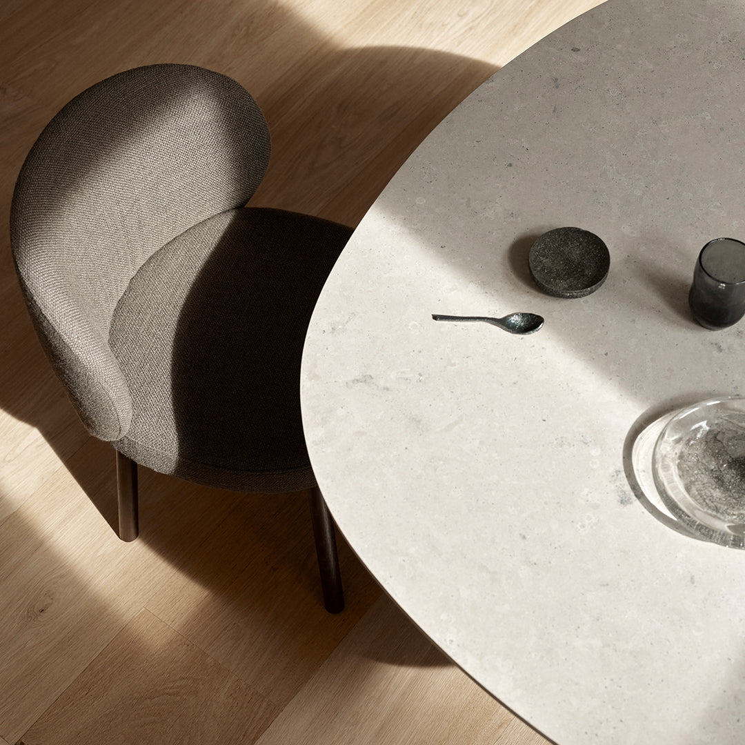Gray upholstered chair beside a smooth, light-colored stone table, featuring subtle patterns and warm wood flooring.