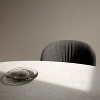 Gray textured chair against a soft beige wall, with a clear glass dish on a light stone table.