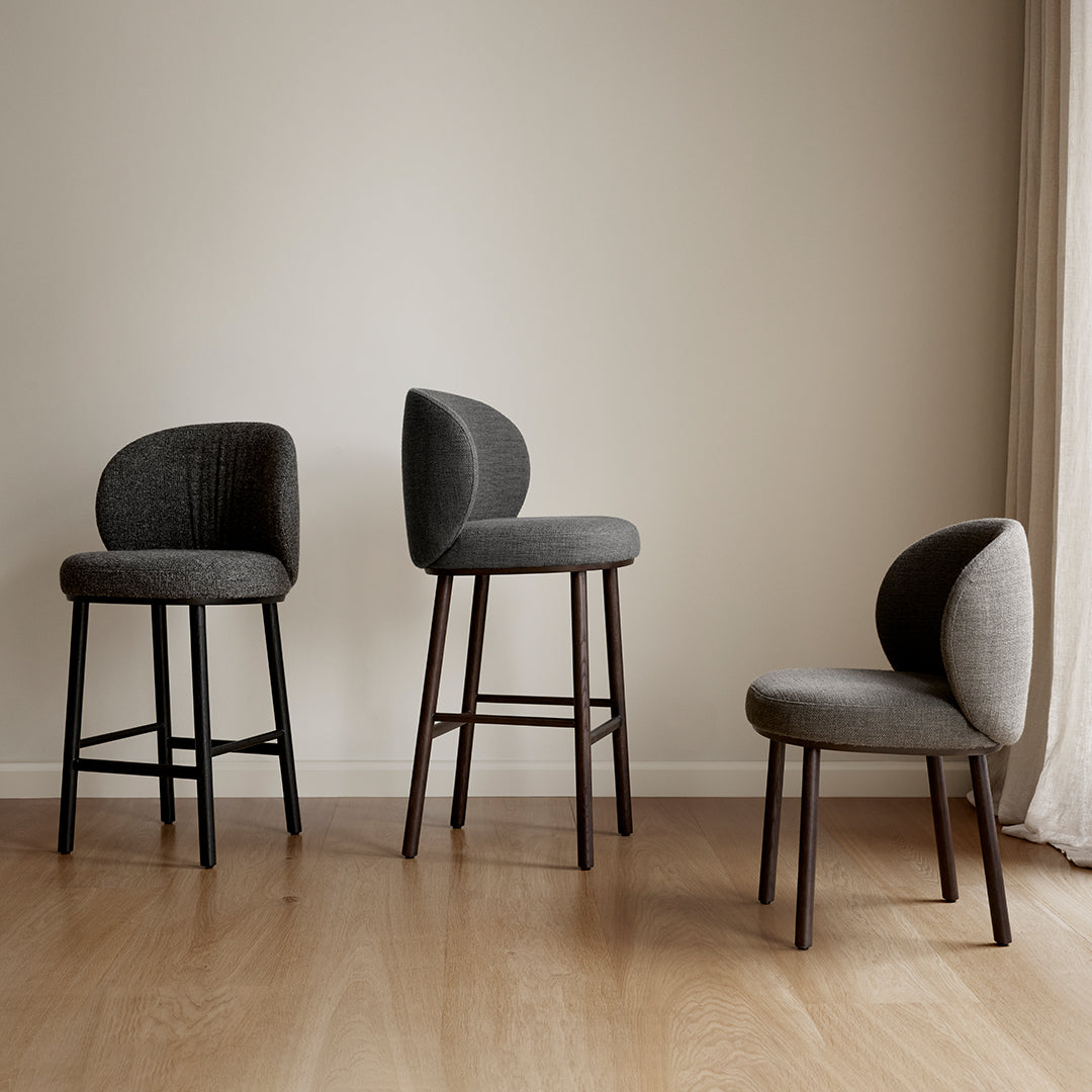 Three upholstered gray stools with curved backs and wooden legs, set against a neutral background. Elegant and modern design.
