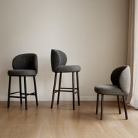 Three upholstered gray stools with curved backs and wooden legs, set against a neutral background. Elegant and modern design.
