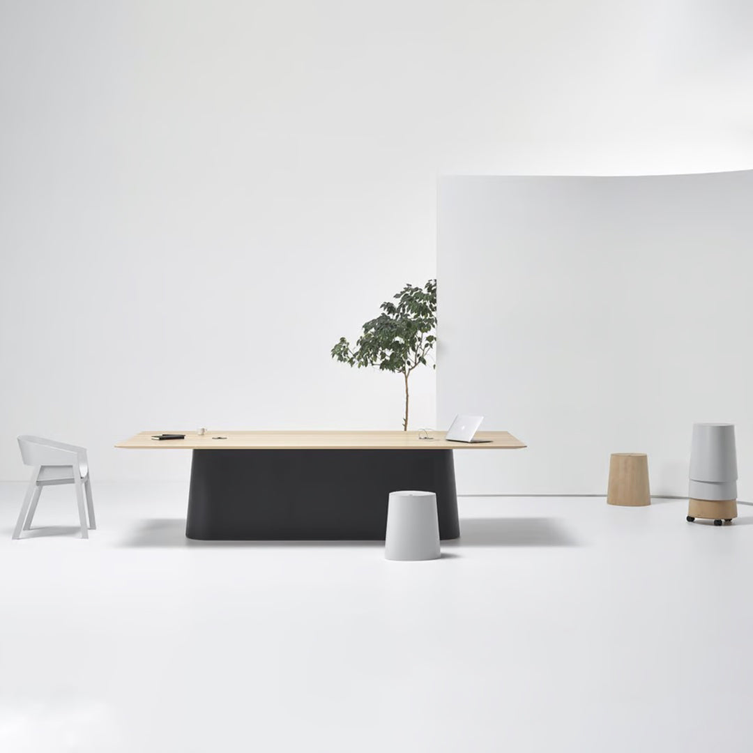Minimalist office setup featuring a wooden tabletop, gray base, white walls, and neutral-toned accent furniture.
