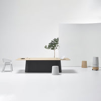 Minimalist office setup featuring a wooden tabletop, gray base, white walls, and neutral-toned accent furniture.