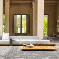 Modern gray sectional sofa with light wood accents and sleek coffee tables on textured gray tiles.