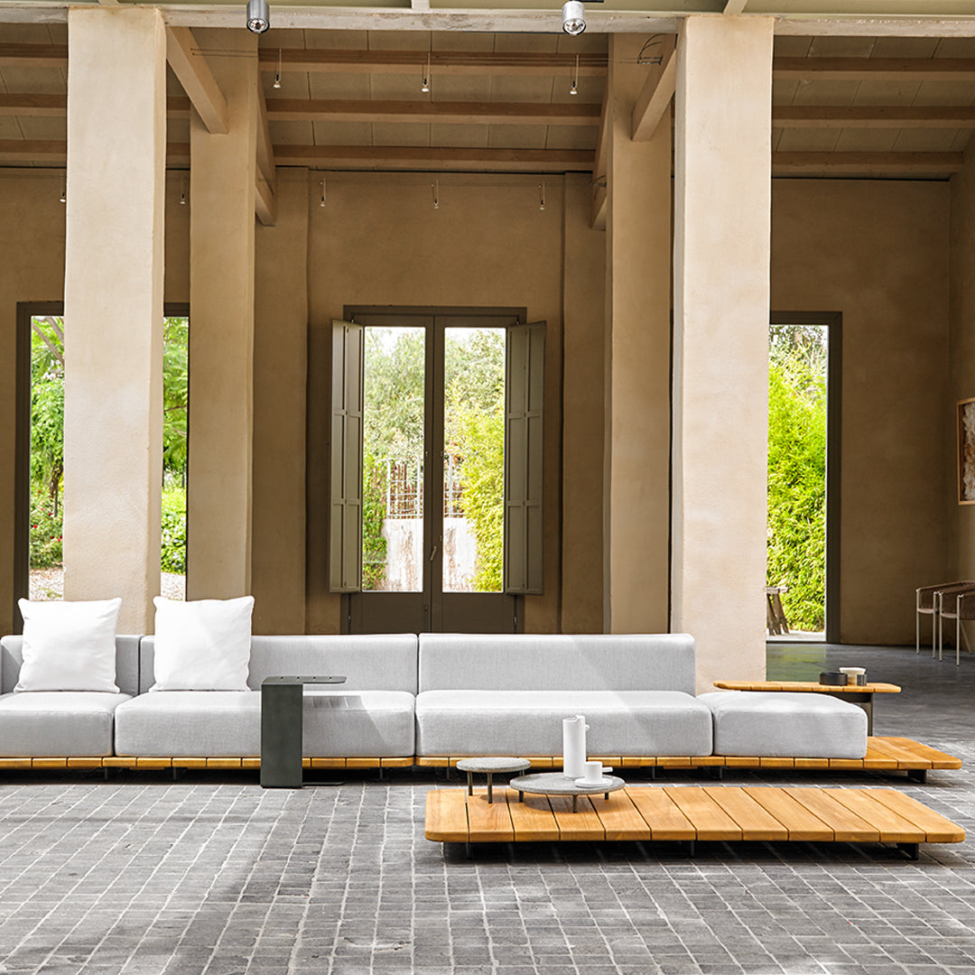 Modern gray sectional sofa with white cushions, accented by natural wood coffee tables in a minimalist setting.