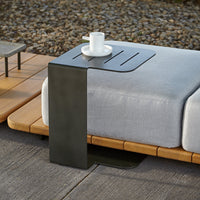 Modern black metal side table with a sleek design, paired with a light gray cushion and natural wood accents.
