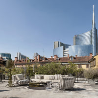 Striped beige and gray outdoor sofa set with a gold and clear lucite accent table against a city skyline backdrop.