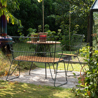 Black metal outdoor bench with wooden slats, set in a lush green garden with vibrant plants in the background.