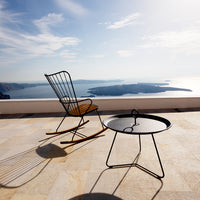 Black metal rocking chair and table with natural wood accents against a serene blue ocean backdrop.