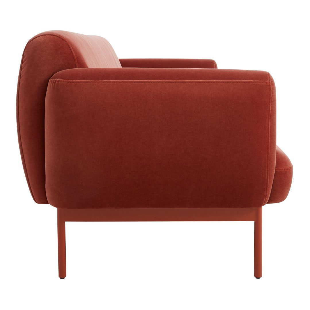 Side view of a rich burnt orange velvet armchair with smooth contours and minimalist metal legs.