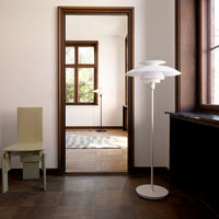 White modern lamp with layered shade design, set against neutral walls and wooden floors.