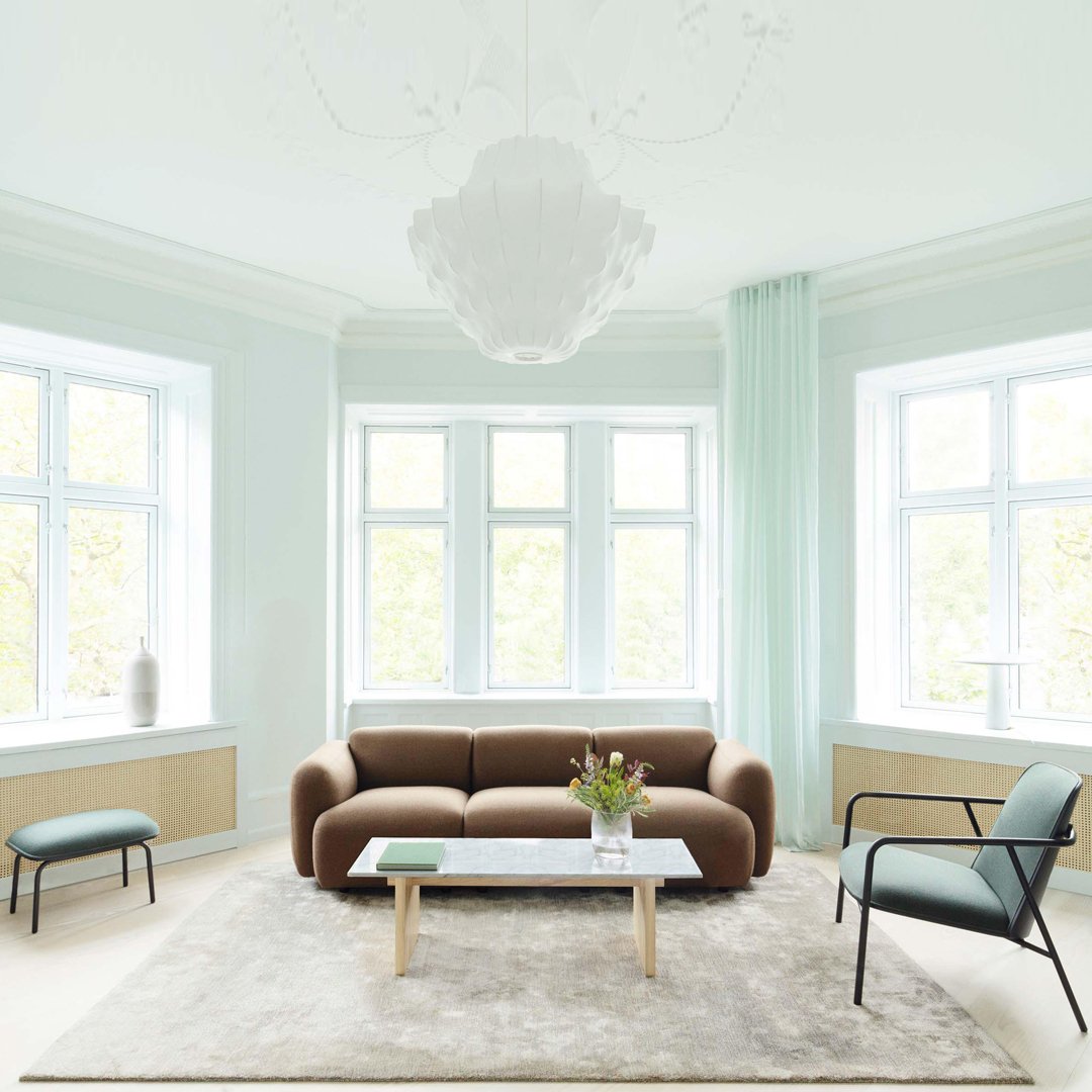 Modern living room with a brown sofa, mint-green accents, a light gray rug, and large windows for natural light.