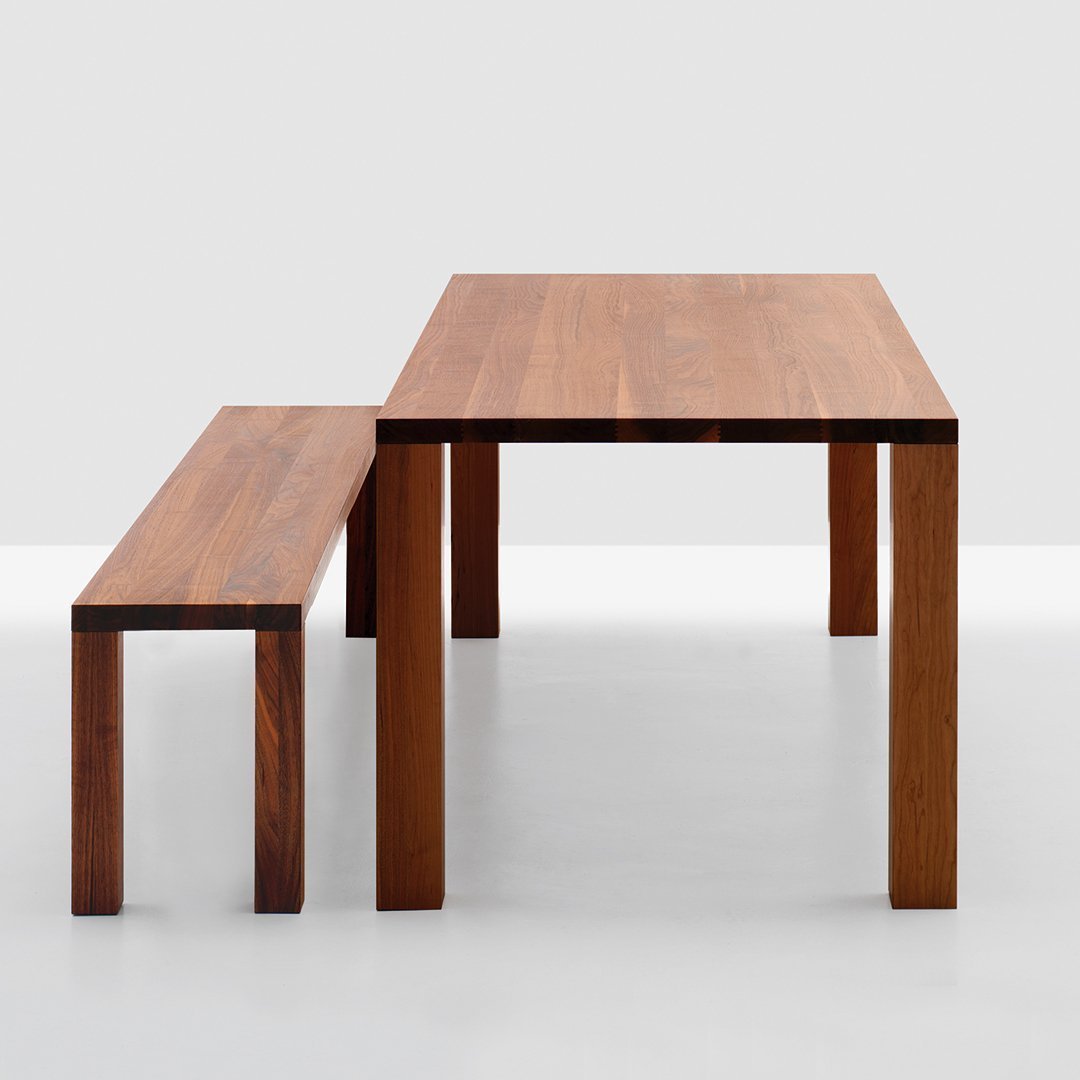 Wooden dining table and bench in warm brown tones, featuring a sleek, minimalist design with straight lines.