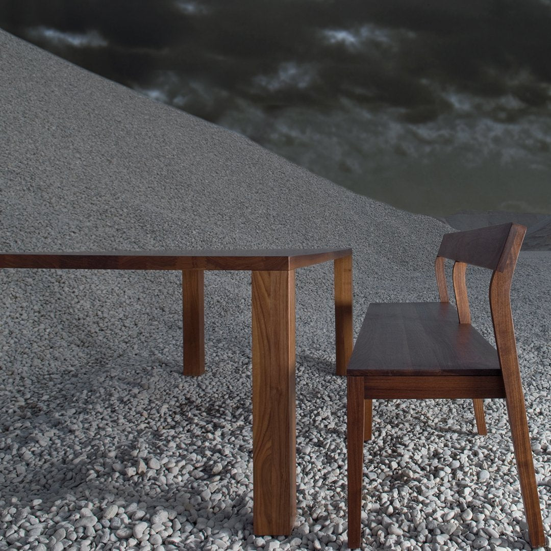 Elegant dark wood table and chair set against a textured gray gravel background, showcasing rich brown tones and clean lines.