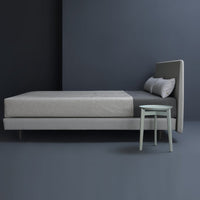 Gray upholstered bed with sleek design, paired with a mint green nightstand against a dark gray wall.