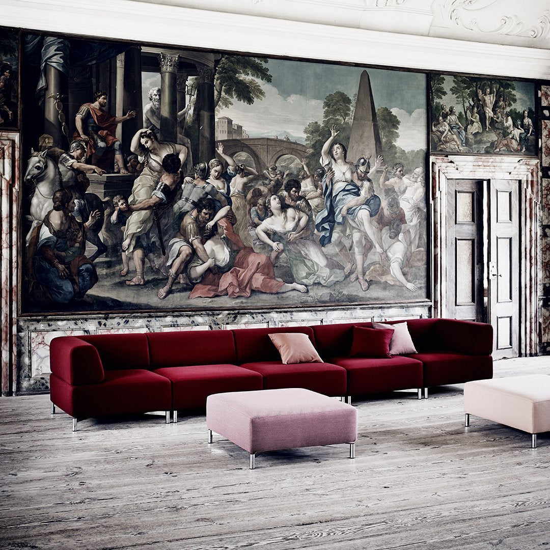 "Deep red sectional sofa with a sleek, modern design against a vintage mural backdrop; minimalist pink accent cushions."