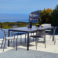 Outdoor dining set featuring a sleek gray table and patterned gray and white chairs against a serene coastal backdrop.