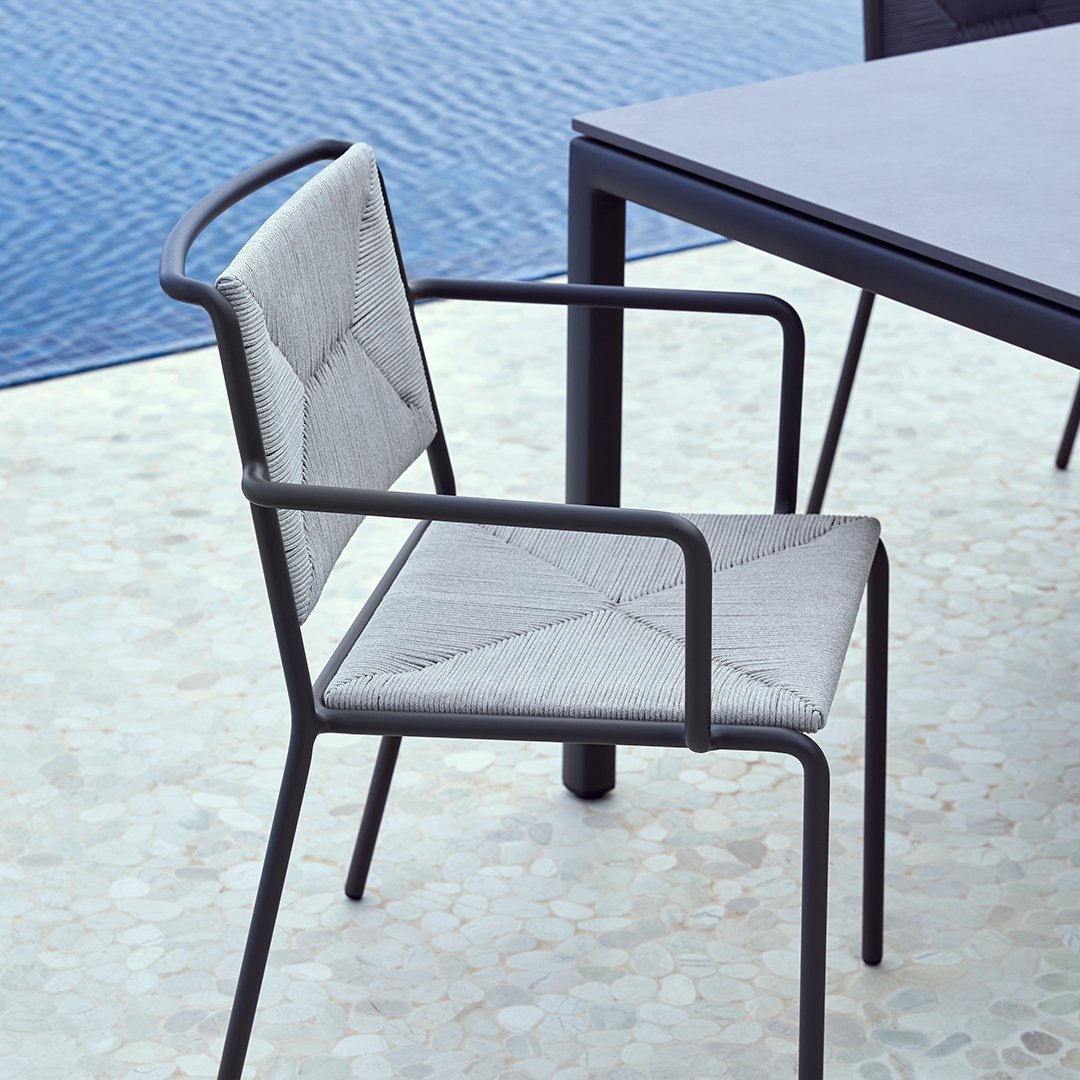 Gray quilted fabric chair with black metal frame, set against a blue water backdrop. Modern outdoor design.