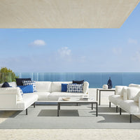 Stylish outdoor sofa set with white fabric, navy blue accents, and a textured gray rug against a serene ocean backdrop.