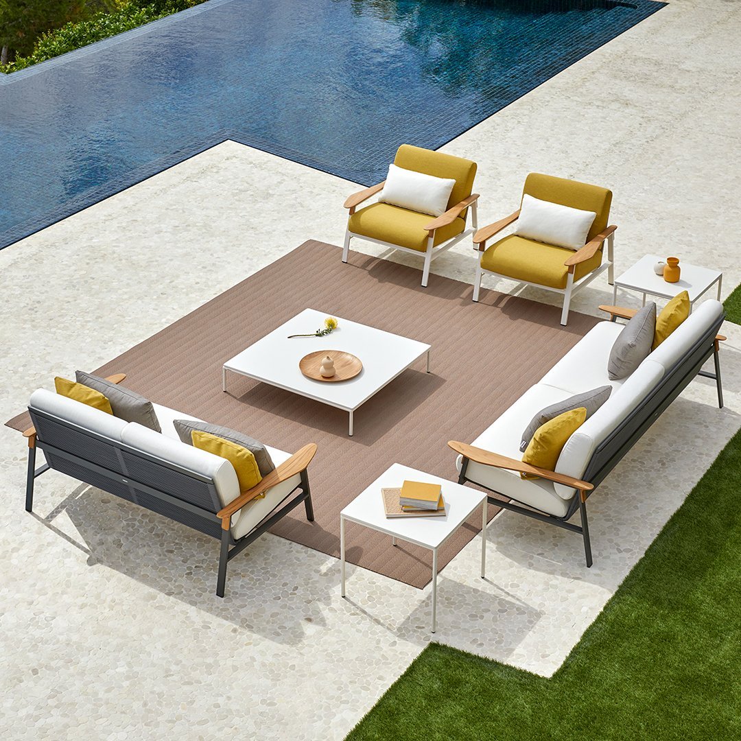 "Modern outdoor seating in gray and white with yellow cushions, featuring a textured brown rug and minimalist white table."