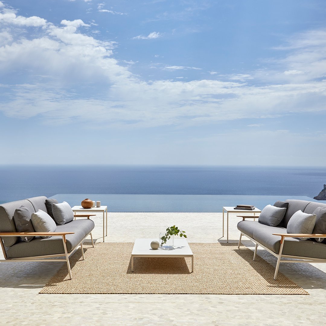 Gray outdoor couches with sleek lines, accentuated by a beige rug and blue ocean backdrop under a bright sky.