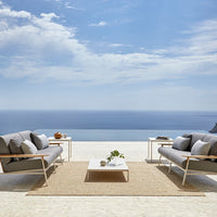 Gray outdoor couches with sleek lines, accentuated by a beige rug and blue ocean backdrop under a bright sky.