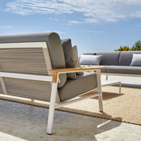 Gray outdoor sofa with wood accents and slatted back, set against a bright blue sky and neutral area rug.