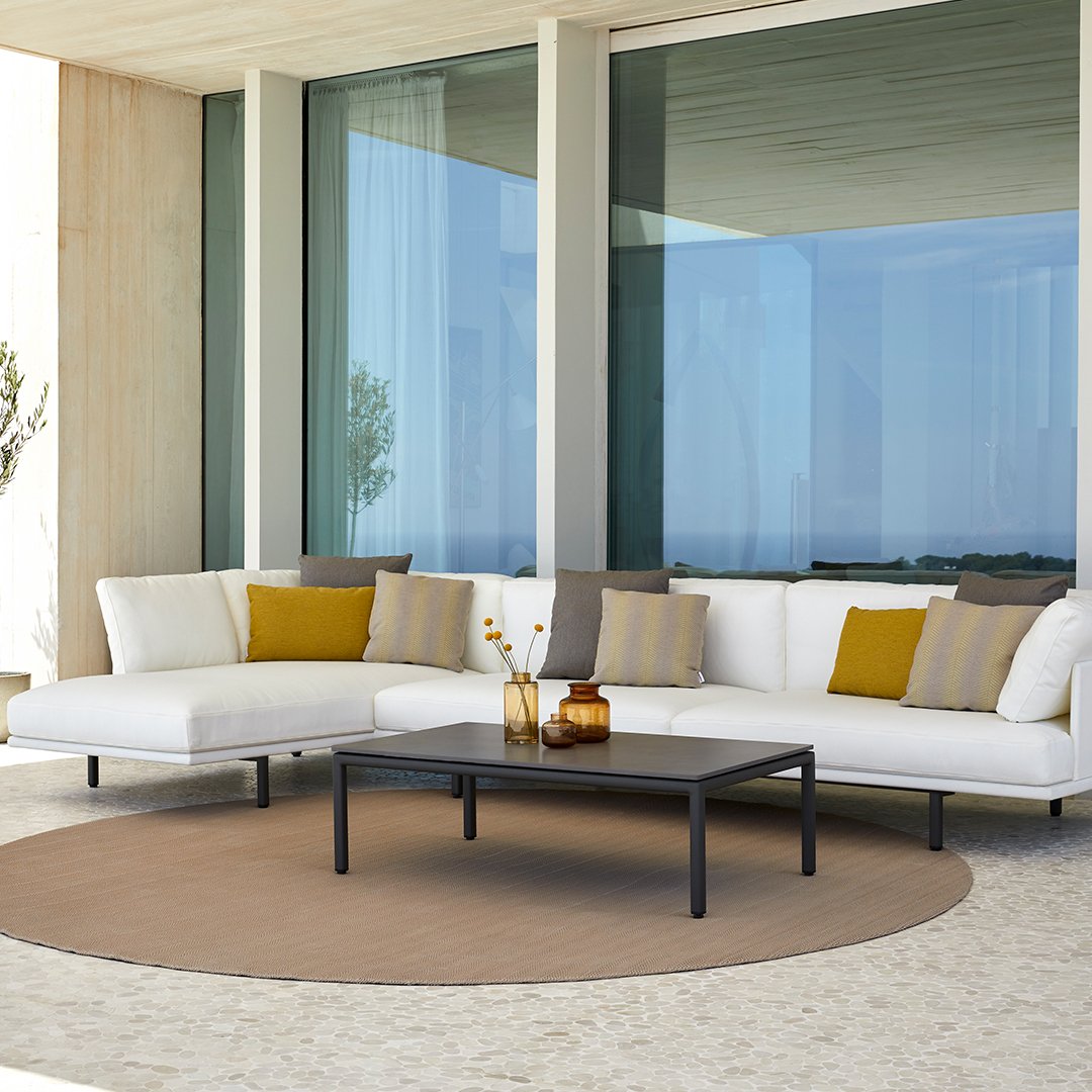 Modern outdoor sofa with white cushions, mustard and gray accent pillows, and a round beige rug.