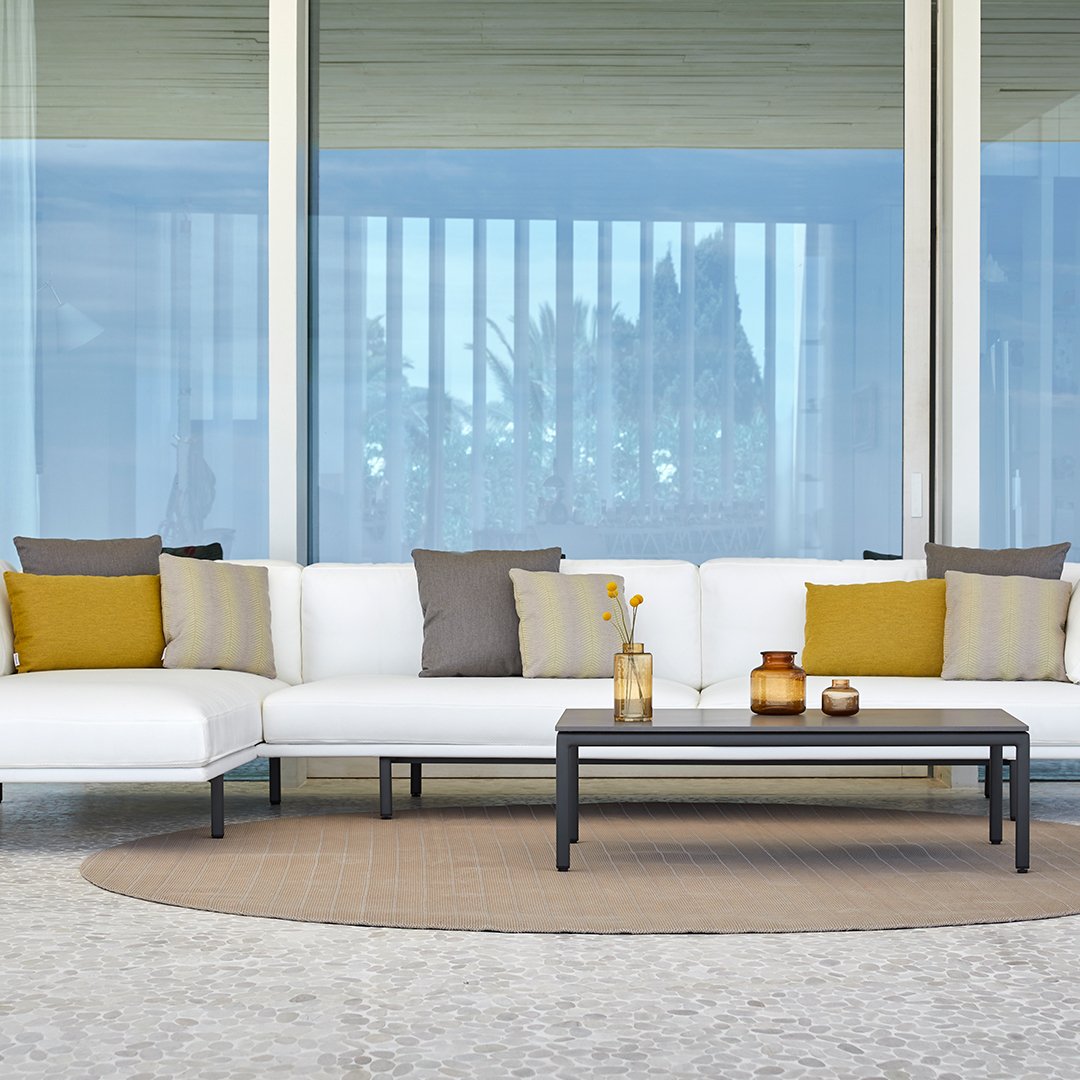 Modern outdoor sectional sofa with white upholstery, gray and mustard cushions, and a round beige rug.