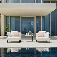 White lounge chairs with coral accents, set against modern architecture and a tranquil pool backdrop.