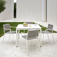 Outdoor dining set featuring a white table and gray woven chairs, set against a minimalist green and stone backdrop.