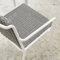 Gray woven pattern on a chair seat with a white frame, set against a light pebble floor.