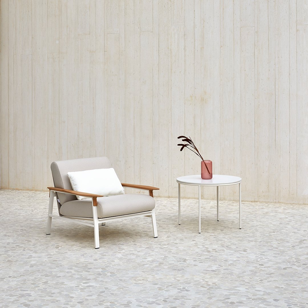 Light beige armchair with wooden accents, paired with a sleek white side table and a soft pink vase. Modern minimalist design.