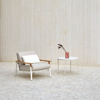 Light beige armchair with wooden accents, paired with a sleek white side table and a soft pink vase. Modern minimalist design.