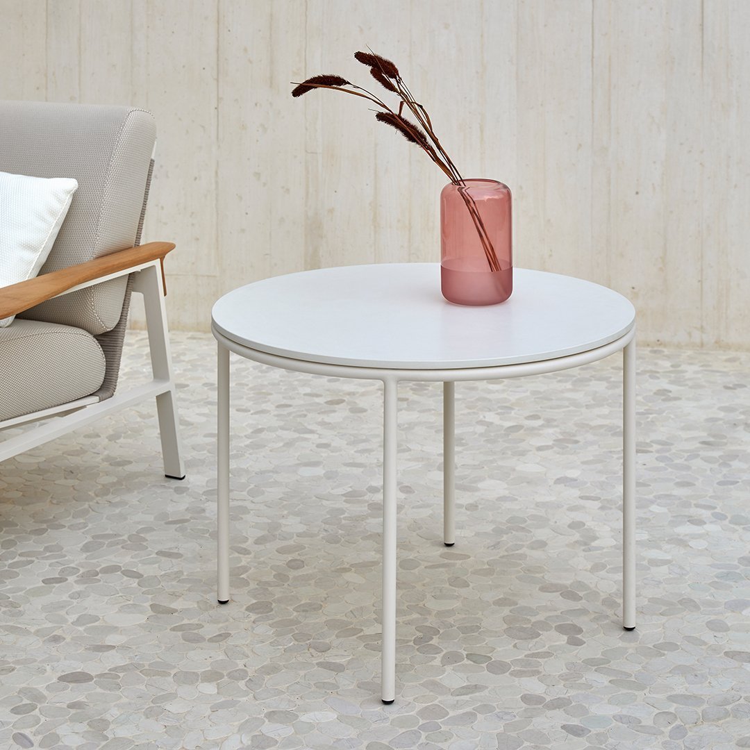 Round white coffee table with sleek metal legs, paired with a textured beige floor and soft pastel decor.